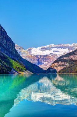 Lake Louise in Banff National Park with its glacier-fed turquoise lakes and Mount Victoria Glacier in the background. Visitors paddling red canoes in the distance. clipart
