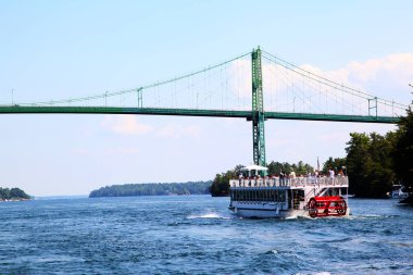 A cruise boat approaches the Thousand Islands International Bridge on the St. Lawrence River connecting New York, USA, with Ontario, Canada in the middle of the 1000 Islands region. clipart