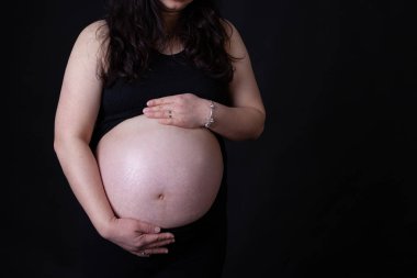 Genç Asyalı hamile anne bebeğini kopya alanı ile mide tutan elleri olan. Siyah arka plan üzerine izole.