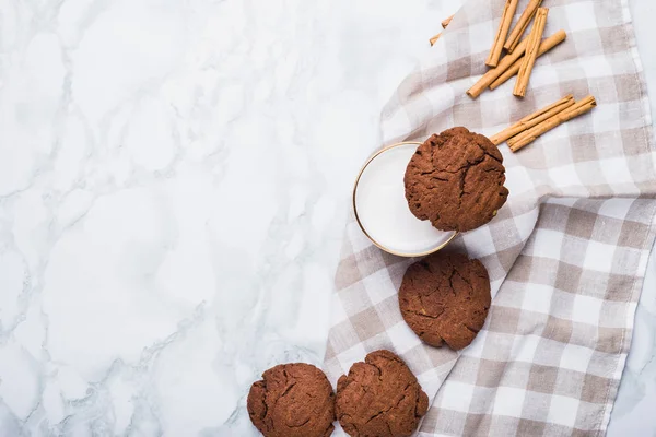 Chocolate vegan cookies, a glass of almond milk, and cinnamon sticks, top view