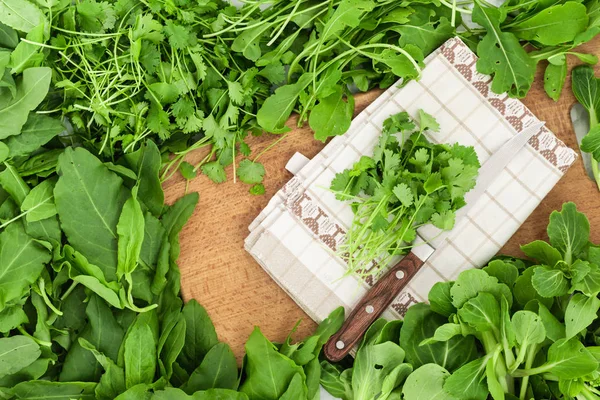 Heaps of fresh parsley, sorrel, rocket salad, and bok choy cabbage leaves spread out around wooden cutting board with parsley on it.
