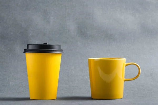 Ceramic mug and single-use cup on a grey background. Lifestyle choice concept