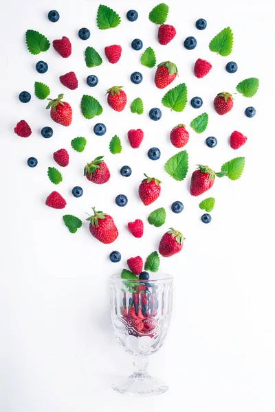 Fresh strawberries, blueberries, and mint leaves flying from a glass, summertime concept