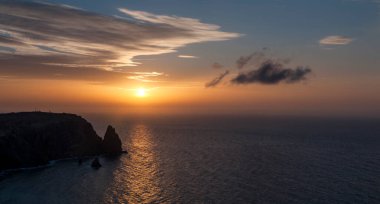 Güneşli bir yolu olan kayalık bir pelerinin üzerinde gün batımı