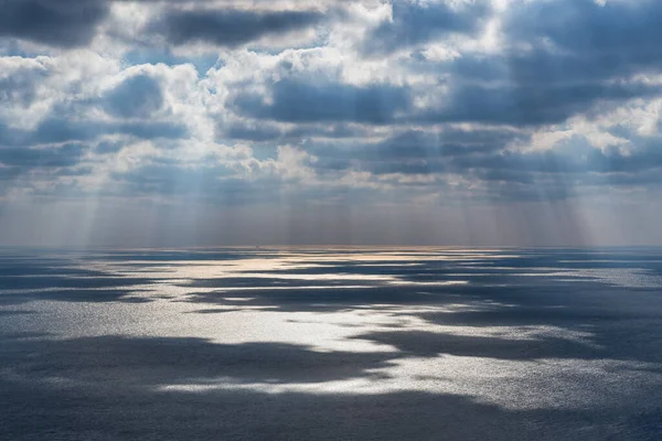 Sun rays through clouds over the sea with reflection
