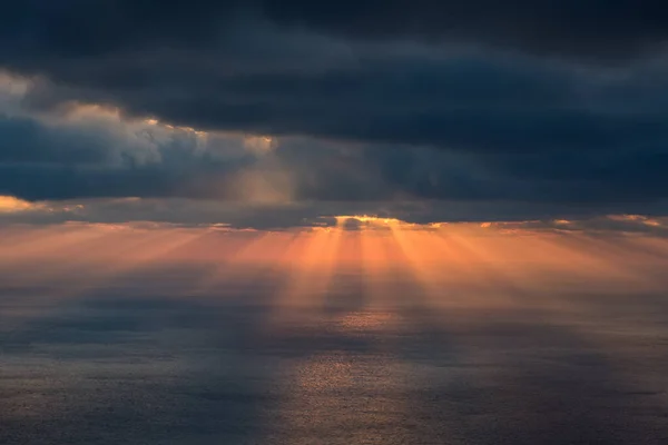 Оранжевые Лучи Заходящего Солнца Сквозь Темные Тучи Над Морем — стоковое фото