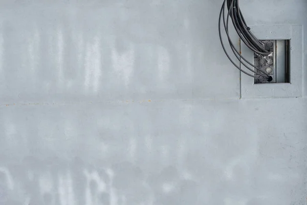 Sağ üst köşesinde siyah kablolar olan boş gri bir duvar var.