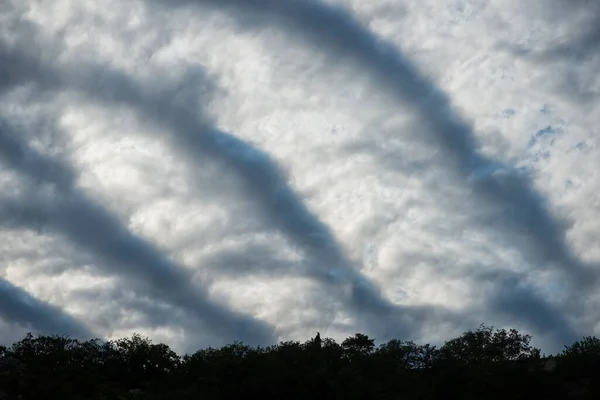 Overcast sky with a recurring stripe pattern clouds over dark wooded area