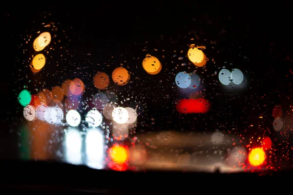 Arabanın ön camında yağmur damlalarıyla yol trafiğinin Bokeh manzarası