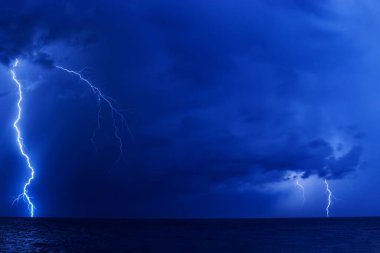 Karanlık gecede denizin üzerinde birkaç şimşek çakar