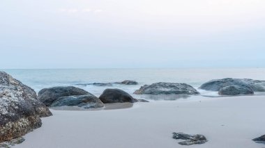Şafak vakti sıcacık bir denizin kıyısında, güzel bir kıyı kayaları manzaralı.