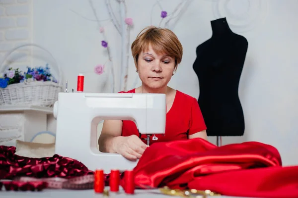 一个穿红衣服的女裁缝在缝纫机上缝制 工作室 裁剪过程 — 图库照片