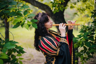 Kraliçe ile elleri bir flüt. Taç güzel kızı boru üzerinde çalış. Fantezi. Altın nakış ile Ortaçağ siyah ve kırmızı elbise.