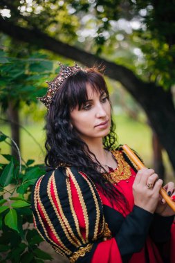 Kraliçe ile elleri bir flüt. Taç güzel kızı boru üzerinde çalış. Fantezi. Altın nakış ile Ortaçağ siyah ve kırmızı elbise.