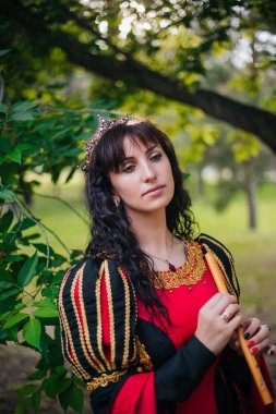 Kraliçe ile elleri bir flüt. Taç güzel kızı boru üzerinde çalış. Fantezi. Altın nakış ile Ortaçağ siyah ve kırmızı elbise.