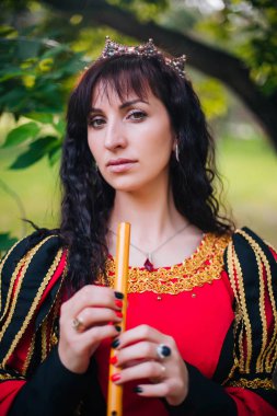 Kraliçe ile elleri bir flüt. Taç güzel kızı boru üzerinde çalış. Fantezi. Altın nakış ile Ortaçağ siyah ve kırmızı elbise.