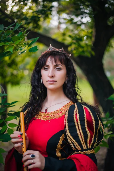 Kraliçe ile elleri bir flüt. Taç güzel kızı boru üzerinde çalış. Fantezi. Altın nakış ile Ortaçağ siyah ve kırmızı elbise.