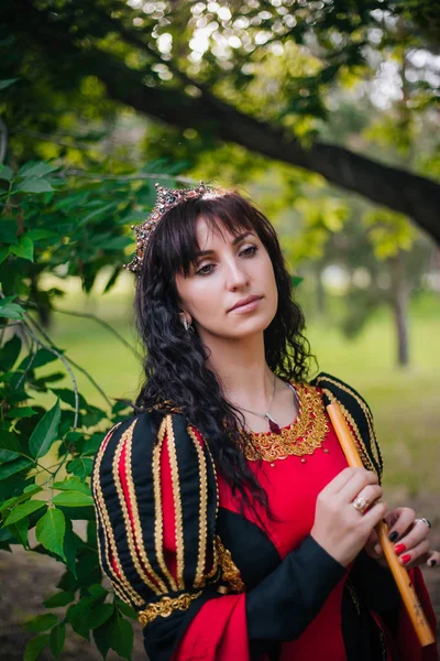 Kraliçe ile elleri bir flüt. Taç güzel kızı boru üzerinde çalış. Fantezi. Altın nakış ile Ortaçağ siyah ve kırmızı elbise.