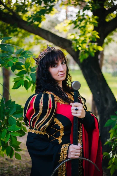Kraliçe onu elinde bir kılıç ile. Taç güzel kız. Fantezi. Altın nakış ile Ortaçağ siyah ve kırmızı elbise.