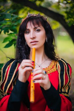 Kraliçe ile elleri bir flüt. Taç güzel kızı boru üzerinde çalış. Fantezi. Altın nakış ile Ortaçağ siyah ve kırmızı elbise.