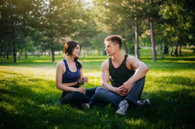 Genç bir kız ve bir erkek çimenlerin üzerinde oturan ve konuşuyor. Açık havada spor yapıyor. Spor giyim insanlar jimnastik yapmak. Spor sonra dinlenme