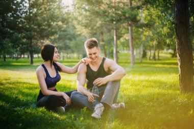Genç bir kız ve bir erkek çimenlerin üzerinde oturan ve konuşuyor. Açık havada spor yapıyor. Spor giyim insanlar jimnastik yapmak. Spor sonra dinlenme