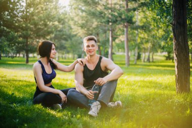 Genç bir kız ve bir erkek çimenlerin üzerinde oturan ve konuşuyor. Açık havada spor yapıyor. Spor giyim insanlar jimnastik yapmak. Spor sonra dinlenme