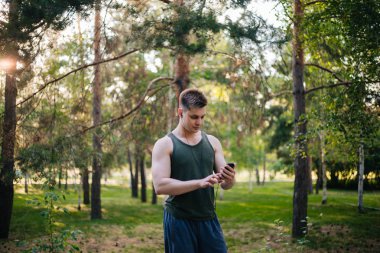 Yakışıklı genç bir adam. Müzik üstünde senin smartphone seçer. Kulaklıklar ve bir cep telefonu ile bir adam.