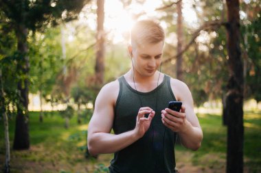 Yakışıklı genç bir adam. Müzik üstünde senin smartphone seçer. Kulaklıklar ve bir cep telefonu ile bir adam.