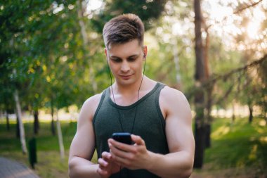 Yakışıklı genç bir adam. Müzik üstünde senin smartphone seçer. Kulaklıklar ve bir cep telefonu ile bir adam.