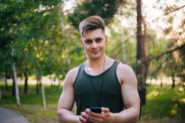 Yakışıklı genç bir adam. Müzik üstünde senin smartphone seçer. Kulaklıklar ve bir cep telefonu ile bir adam.