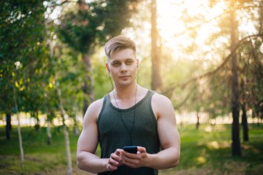 Yakışıklı genç bir adam. Müzik üstünde senin smartphone seçer. Kulaklıklar ve bir cep telefonu ile bir adam.