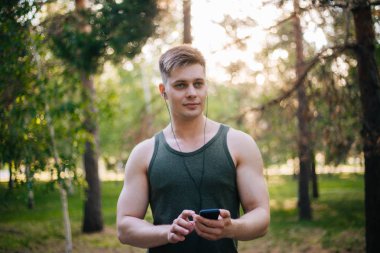 Yakışıklı genç bir adam. Müzik üstünde senin smartphone seçer. Kulaklıklar ve bir cep telefonu ile bir adam.