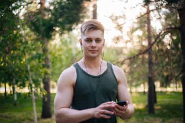 Yakışıklı genç bir adam. Müzik üstünde senin smartphone seçer. Kulaklıklar ve bir cep telefonu ile bir adam.