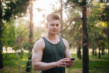 Yakışıklı genç bir adam. Müzik üstünde senin smartphone seçer. Kulaklıklar ve bir cep telefonu ile bir adam.