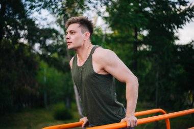 Genç yakışıklı olan bir spor yatay çubuklar üzerinde çalışmaktadır. Sağlıklı yaşam tarzı