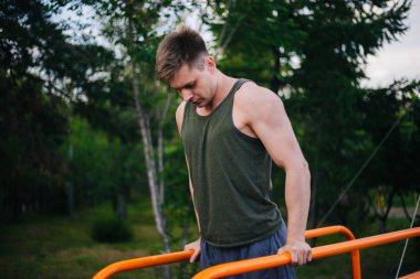 Genç yakışıklı olan bir spor yatay çubuklar üzerinde çalışmaktadır. Sağlıklı yaşam tarzı