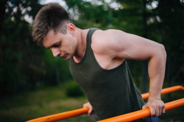 Genç yakışıklı olan bir spor yatay çubuklar üzerinde çalışmaktadır. Sağlıklı yaşam tarzı