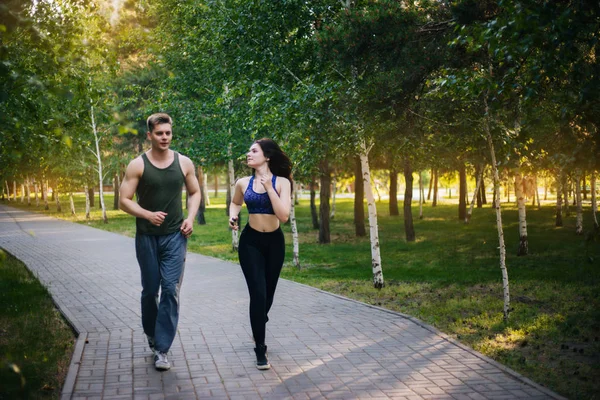 A young girl and a guy are running around the park. Doing sports outdoors. People in sportswear make a run. Leisure