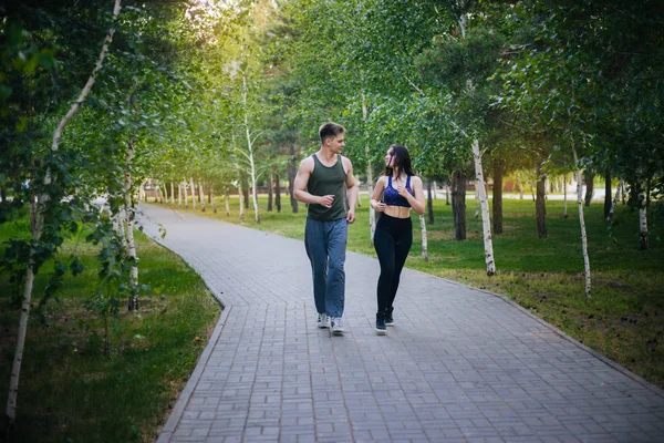 A young girl and a guy are running around the park. Doing sports outdoors. People in sportswear make a run. Leisure