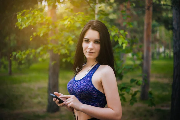 Genç güzel kız ile hareket eden telefon. Spor giyim onun elinde bir akıllı telefon ile kulaklıklar giyen bir kadın. Sağlıklı bir yaşam tarzı. Müzik.