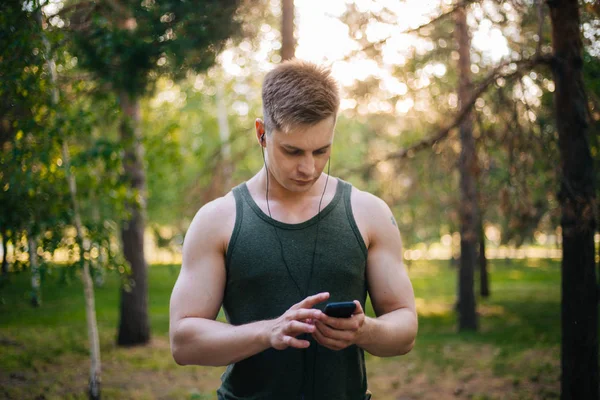 Yakışıklı genç bir adam. Müzik üstünde senin smartphone seçer. Kulaklıklar ve bir cep telefonu ile bir adam.