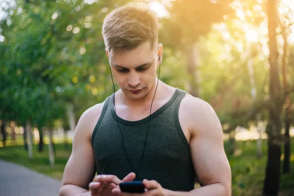 Yakışıklı genç bir adam. Müzik üstünde senin smartphone seçer. Kulaklıklar ve bir cep telefonu ile bir adam.