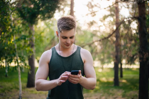 Yakışıklı genç bir adam. Müzik üstünde senin smartphone seçer. Kulaklıklar ve bir cep telefonu ile bir adam.