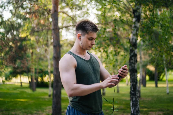 Yakışıklı genç bir adam. Müzik üstünde senin smartphone seçer. Kulaklıklar ve bir cep telefonu ile bir adam.