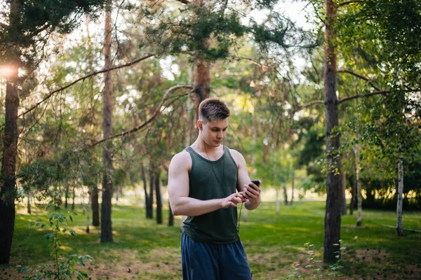 Yakışıklı genç bir adam. Müzik üstünde senin smartphone seçer. Kulaklıklar ve bir cep telefonu ile bir adam.