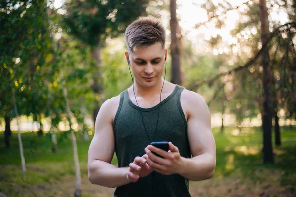 Yakışıklı genç bir adam. Müzik üstünde senin smartphone seçer. Kulaklıklar ve bir cep telefonu ile bir adam.