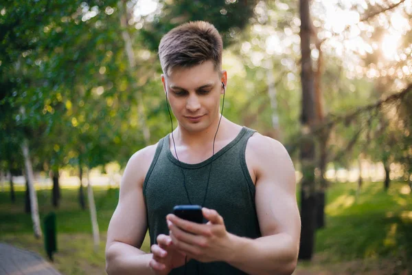 Yakışıklı genç bir adam. Müzik üstünde senin smartphone seçer. Kulaklıklar ve bir cep telefonu ile bir adam.