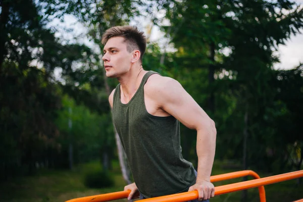 Genç yakışıklı olan bir spor yatay çubuklar üzerinde çalışmaktadır. Sağlıklı yaşam tarzı
