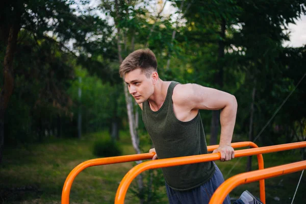 Genç yakışıklı olan bir spor yatay çubuklar üzerinde çalışmaktadır. Sağlıklı yaşam tarzı